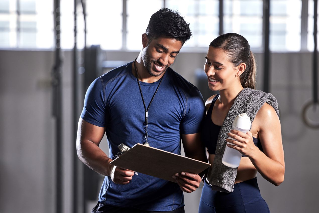 Trainer gibt einer Kundin Trainingsanweisungen im Fitnessstudio fuer nachhaltige Fitness mit personal trainer koeln