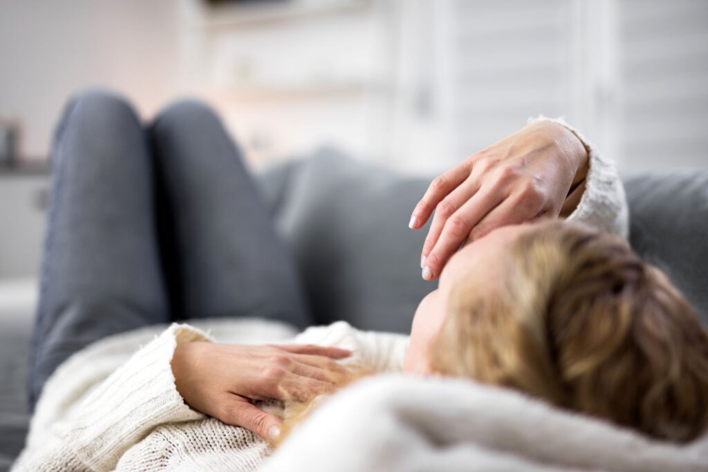 Frau liegt erschöpft auf dem Sofa und erholt sich nach Krankheit – Symbol fuer Ruhe und Heilungszeit mit Unterstuetzung durch den Pflegedienst Bielefeld.